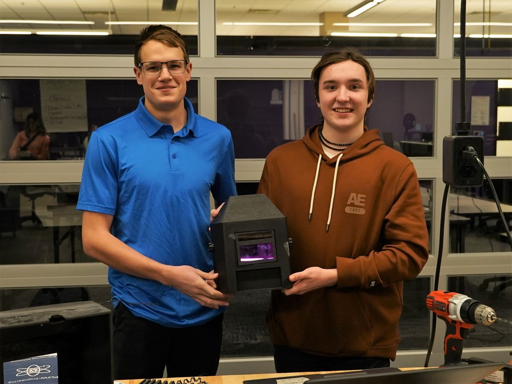 Two students proudly holding up their 3D printed welding helmet prototype